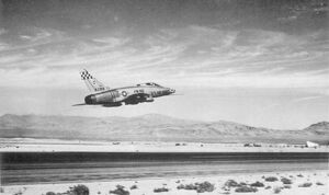 Rear quarter view of a jet fighter taking off with mountainous terrain visible in the distance